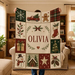 May include: A rectangular throw blanket featuring a cream-colored center with the name OLIVIA in red letters, surrounded by a grid of Christmas-themed illustrations including a red truck, gingerbread man, snowman, and pine trees.