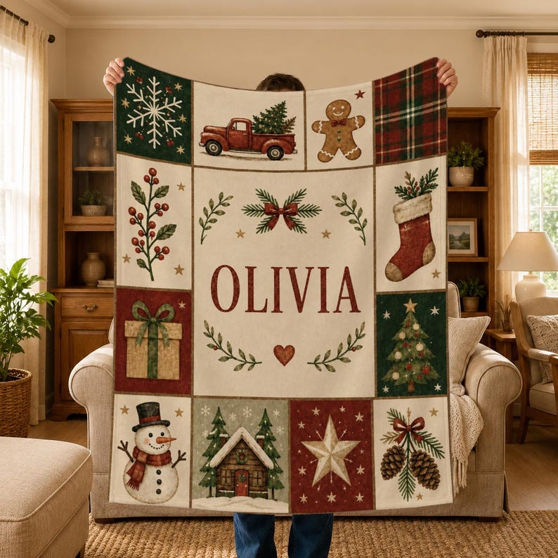 May include: A rectangular throw blanket featuring a cream-colored center with the name OLIVIA in red letters, surrounded by a grid of Christmas-themed illustrations including a red truck, gingerbread man, snowman, and pine trees.