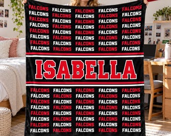 May include: A black fleece blanket featuring a repeating pattern of the word FALCONS in white and red text. A central horizontal band displays the name ISABELLA in large red capital letters with a white outline against a black background.