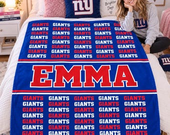 May include: A blue fleece blanket featuring a repeating pattern of the word GIANTS in white and red text, with the name EMMA printed in large red letters across the center. The blanket is displayed on a bed with pillows and a matching throw pillow.
