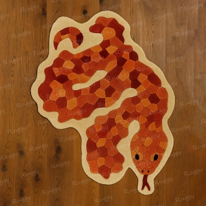 Può includere: Un tappeto a forma di serpente con un bordo beige e un corpo composto da forme geometriche arancioni e rosse. Il tappeto ha una testa dettagliata con occhi neri e una lingua rossa. Il tappeto è posto su un pavimento in legno.