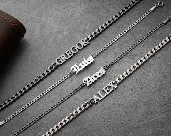 May include: Four silver-toned name bracelets with curb chains. The names "Gregor", "Luts", "Ares", and "Alex" are displayed in various fonts. The bracelets are arranged diagonally against a gray background.