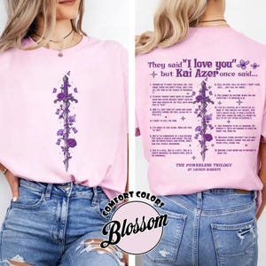 Może przedstawiać: Jasnoróżowa koszulka z fioletowym kwiatowym i mieczowym wzorem z przodu i z tyłu. Tył koszulki zawiera tekst "They said 'I love you' but Kai Azer once said..." oraz listę cytatów. Koszulka jest częścią "The Powerless Trilogy" autorstwa Lauren Roberts.