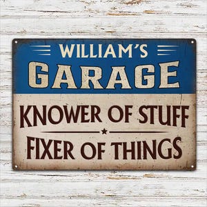 Pode incluir: Uma placa retangular de metal com uma seção superior azul e uma seção inferior creme. O texto diz WILLIAM'S GARAGE em azul e creme, seguido por KNOWER OF STUFF e FIXER OF THINGS em letras castanho-escuras com uma pequena estrela central.