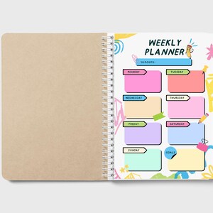 May include: Open weekly planner with a spiral binding. The left page is blank, while the right page features a colorful layout with the words "WEEKLY PLANNER." It includes boxes for each day of the week and a section for goals.