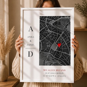 Könnte beinhalten: Ein gerahmtes vertikales Wandbild mit einem dunkelgrauen Stadtplan und einem roten Herzsymbol. Der Text lautet A, ANIKA & DANIEL, D sowie WO ALLES BEGANN 22.07.2016 BERLIN 53 07'38.8"N 4 12'60.8"E. Der Rahmen ist weiß und rechteckig.