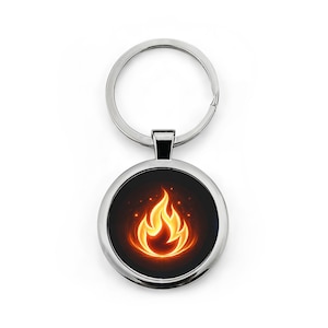 May include: A circular, silver keyring featuring a black backdrop and a stylized orange and yellow flame design. The keyring has a split ring for attaching keys and a small rectangular connector.