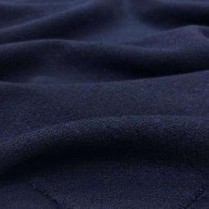 May include: Close-up of a navy blue fabric with a textured surface. The fabric is draped, showing soft folds and shadows. The material appears to be a medium-weight textile, suitable for apparel or home decor.