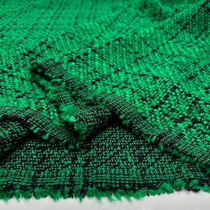 May include: Close-up of a textured fabric with a woven pattern. The fabric is primarily bright green with black flecks and a fringed edge. The weave creates a slightly raised, tactile surface.