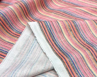 May include: Close-up of a fabric with a striped pattern in shades of pink, orange, blue, and black. The fabric is folded over, revealing a white underside. The stripes run vertically, creating a wavy effect.