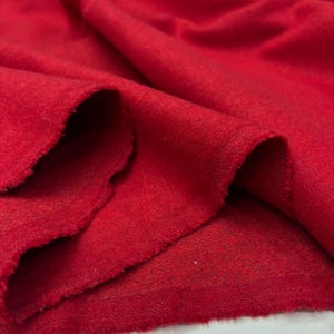 May include: A vibrant red fabric with a soft, fuzzy, and slightly textured surface. The material is draped in loose folds, showcasing its thick, opaque quality and consistent deep red color throughout the entire visible piece of textile.