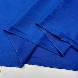 Puede incluir: Primer plano de una tela azul vibrante con textura y pliegues visibles. Los bordes est&aacute;n cuidadosamente acabados con costuras blancas. El color de la tela es un azul rico y saturado, creando una imagen visualmente atractiva.