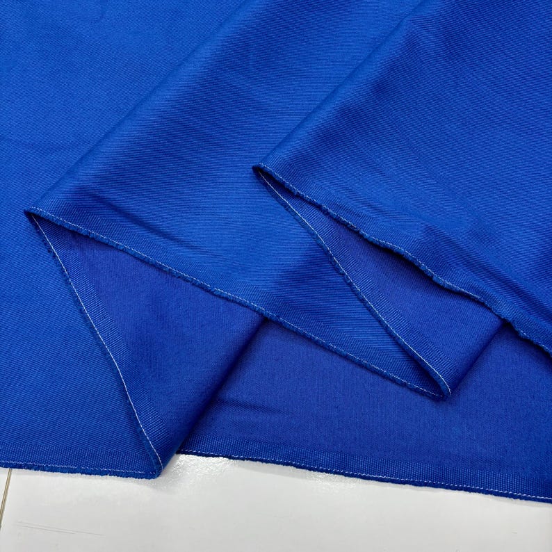 Puede incluir: Primer plano de una tela azul vibrante con textura y pliegues visibles. Los bordes est&aacute;n cuidadosamente acabados con costuras blancas. El color de la tela es un azul rico y saturado, creando una imagen visualmente atractiva.