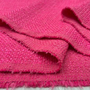 May include: Close-up of a vibrant pink fabric with a textured weave. The fabric has a slightly frayed edge, and the texture is visible throughout the material. The color is a bright, saturated pink.
