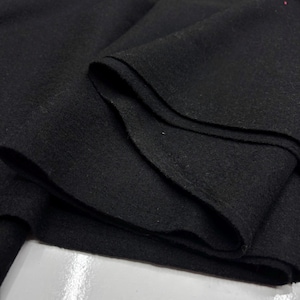 Può includere: Primo piano di un tessuto nero piegato. Il tessuto sembra essere un materiale morbido, con pieghe e strati visibili. Il colore scuro e la consistenza suggeriscono che potrebbe essere utilizzato per abbigliamento o arredamento.