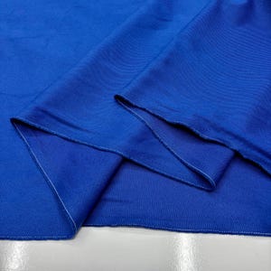 Puede incluir: Primer plano de una tela azul vibrante, mostrando su textura y pliegues. Los bordes est&aacute;n acabados con costuras blancas, creando un aspecto limpio y a medida. La tela parece ser de peso medio, adecuada para diversos proyectos de costura. El color es azul saturado.