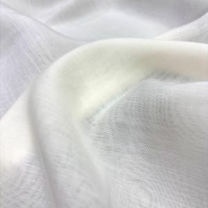 May include: Close-up of a white, sheer fabric with a subtle texture. The fabric is draped, creating soft folds and shadows. The material appears lightweight and slightly translucent, with a gentle sheen.