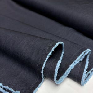 May include: Close-up of dark navy blue fabric with a light blue frayed edge. The fabric is folded, showing the texture and weave of the material. The edges are unfinished, giving it a raw, natural look. Ideal for apparel or home decor.