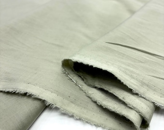May include: Close-up of a folded, light green fabric with a raw, frayed edge. The fabric appears to be lightweight and has small perforations along the edge. The folds create shadows and texture, highlighting the material's drape.