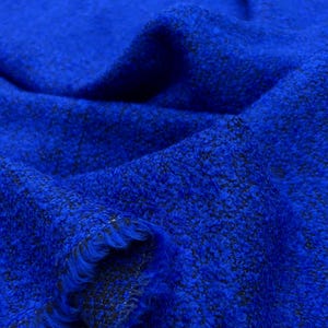 May include: A close-up shot of a bright blue fabric with a textured surface. The material has a woven appearance with darker flecks throughout. The edges of the fabric are frayed, revealing the weave. This textile is suitable for clothing and home decor.