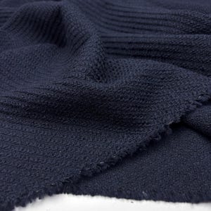 Puede incluir: Una tela de color azul marino oscuro con un tejido texturizado distintivo. El material muestra una combinación de secciones acanaladas horizontales y un patrón de superficie fino y granular. Los bordes del textil parecen deshilachados.