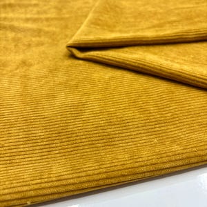 May include: Close-up of folded mustard yellow corduroy fabric. The fabric has a ribbed texture, with the ridges running horizontally. The material is soft and appears new. The colour is a rich, golden yellow.