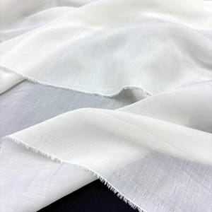 May include: Close-up of white fabric with a delicate, semi-transparent texture. The fabric is draped in soft folds, creating shadows and highlights. The edges of the fabric have a raw, unfinished look. The overall effect is one of lightness and elegance.