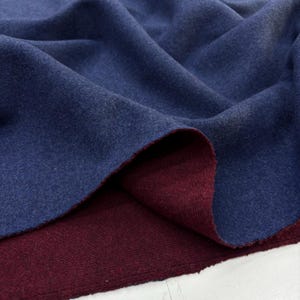 Puede incluir: Primer plano de una tela de dos tonos. La capa superior es azul marino, mientras que la inferior es burdeos. La tela está doblada, revelando ambos colores y texturas. El material parece suave, posiblemente de lana.