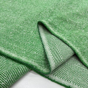 May include: A close-up shot of a green and white herringbone fabric. The fabric is folded, showing the texture and weave. The colour is a vibrant green with white accents, creating a visually appealing textile.