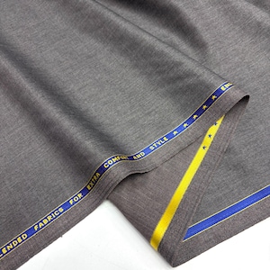 May include: A piece of solid grey fabric with a fine texture. The selvedge edge features a blue border with yellow stars and the printed text "BLENDED FABRICS FOR EXTRA COMFORT AND STYLE". The fabric is folded to reveal the finished edge.