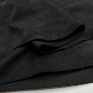 May include: Close-up of black fabric with a soft, textured surface. The fabric is folded over itself, revealing multiple layers. The material appears to be a dark, solid color, possibly a textile for clothing or home decor.