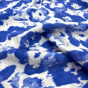 May include: Close-up of a fabric with a blue and white abstract pattern. The fabric has a soft, flowing appearance, with the blue shapes resembling brushstrokes or watermarks. The overall design is modern and artistic.