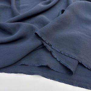 May include: A length of solid slate blue fabric with a soft, matte texture and visible folds. The material features raw, frayed edges along the cut sections, showcasing a loose weave and a consistent, muted blue color throughout the textile.