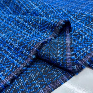 May include: Close-up of a textured fabric with a blue and black woven pattern. The fabric has a herringbone design with a frayed edge. The color palette includes shades of blue, black, and a hint of purple.