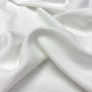 Könnte beinhalten: Nahaufnahme eines weißen Stoffes mit weichen Falten und dezentem Glanz. Das Material wirkt glatt und leicht, mit sichtbarer Textur vom Gewebe. Der Stoff ist einfarbig, strahlend weiß und drapiert sich anmutig.
