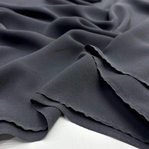 Peut inclure: Gros plan sur un tissu gris foncé à la texture douce et fluide. Le tissu est drapé, révélant des plis et des ombres subtiles. Les bords du tissu sont inachevés, avec un aspect légèrement effiloché. L'ensemble est élégant et lisse.