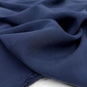 May include: A close-up of navy blue fabric, showing soft folds and a subtle texture. The material looks lightweight and flowing, with a matte finish. The colour is a deep, saturated blue, suitable for clothing or home furnishings.