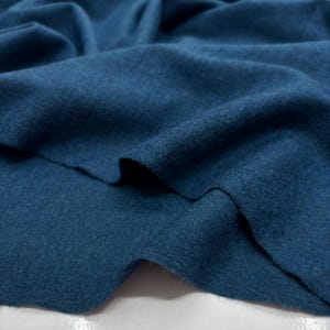 May include: Close-up of a folded piece of teal-colored fabric. The fabric has a soft, textured appearance with visible folds and creases. The color is a deep, saturated teal, with subtle variations in tone across the surface.
