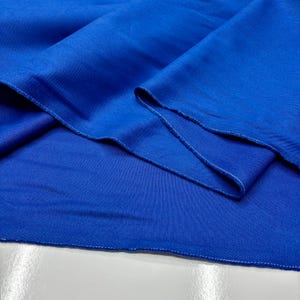 Puede incluir: Primer plano de una tela azul vibrante con textura visible y costuras blancas en los bordes. La tela est&aacute; doblada, mostrando su ca&iacute;da y la calidad del material. El color es un azul rico y saturado.