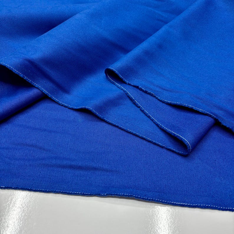 Puede incluir: Primer plano de una tela azul vibrante con textura visible y costuras blancas en los bordes. La tela est&aacute; doblada, mostrando su ca&iacute;da y la calidad del material. El color es un azul rico y saturado.