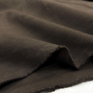 May include: Close-up of a dark brown fabric with visible texture and a raw edge. The fabric is folded, showing the interplay of light and shadow across its surface. The material appears to be a medium-weight textile.