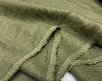 May include: Close-up of olive green linen fabric. The fabric is folded, showing the texture and frayed edges. The color is a muted, earthy green, suitable for clothing or home decor projects.