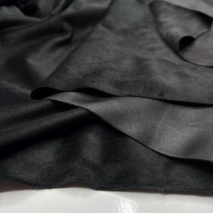 May include: Close-up of a dark grey fabric with a velvety texture. The fabric is layered, revealing a smooth, slightly shiny underside. The folds and shadows create depth and dimension, highlighting the material's luxurious appearance.