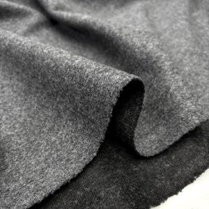 May include: Close-up of a folded piece of gray fabric. The material has a soft, textured appearance with a slightly uneven surface. The fabric's edges are visible, revealing its thickness and construction. The overall tone is neutral, with subtle variations in the gray color.