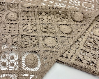 May include: Close-up of a tan crochet textile with a repeating geometric pattern. The design features squares and circles, creating an openwork effect. The fabric is folded, revealing the intricate details of the handmade craft.
