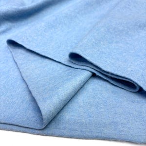 May include: Close-up of a light blue fabric with a soft, textured appearance. The fabric is folded, revealing layers and edges. The colour is a solid, pale blue, and the material appears to be a knit or woven textile.