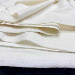 May include: Close-up of folded, off-white fabric. The fabric appears soft and has a slightly textured surface. The layers of fabric are visible, creating a sense of depth and volume. The overall impression is of a clean, simple textile.