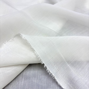 May include: Close-up of white fabric with a textured surface. The fabric is folded, showing the raw edge. The material appears lightweight and semi-sheer, suitable for clothing or home decor. The fabric is draped.