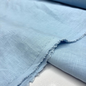 Puede incluir: Primer plano de una tela azul claro con un borde deshilachado. La tela parece ser lino o un material ligero similar, con una superficie ligeramente texturizada. El color es un azul suave y pálido.