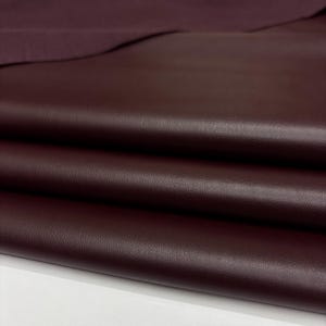 May include: Close-up of burgundy leather fabric. The leather is folded, showing the texture and depth of the material. The colour is a deep, rich shade of red-purple, with subtle variations in tone. The fabric appears smooth and supple, suitable for various crafting projects.